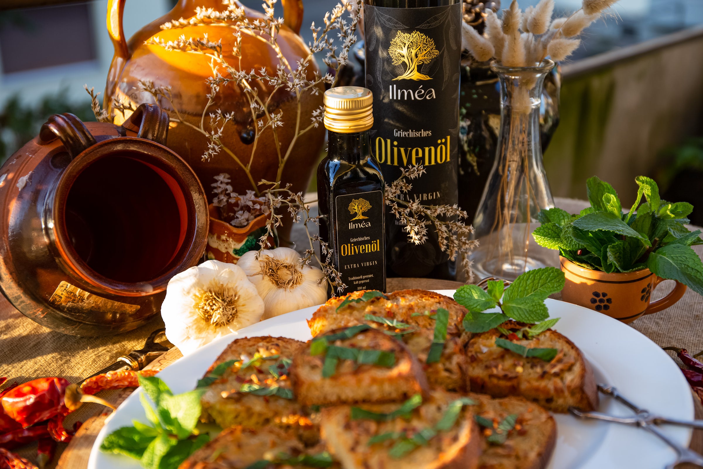 Ilmea Olivenöl in der Abendsonne mit Mediterranem Gericht und feinem Knoblauch.